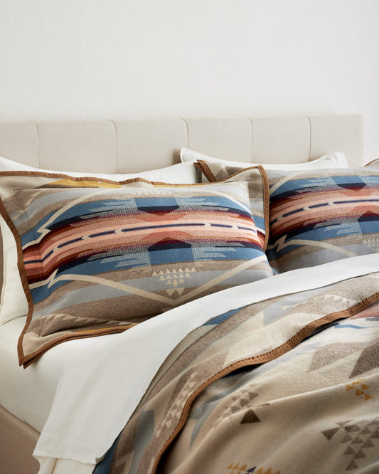 Patterned pillows and blanket on a bed with a neutral headboard