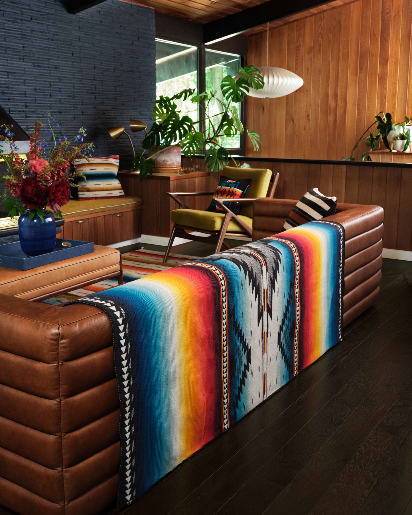 Colorful striped blanket draped over a brown leather sofa in a modern living room.
