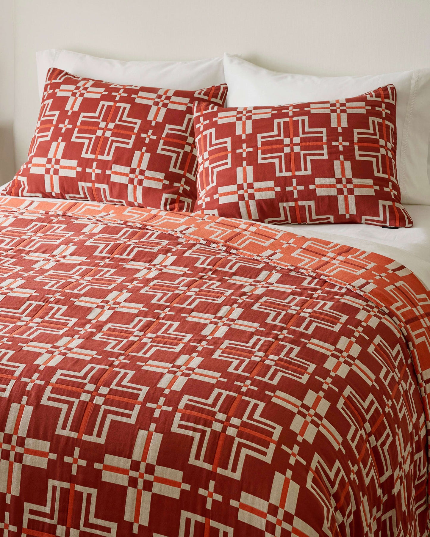 Red and white geometric patterned bedding set on a bed with pillows.