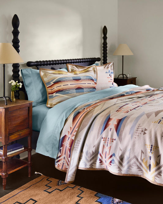 Bedroom with a bed featuring a patterned comforter and pillows, wooden nightstands, and lamps.