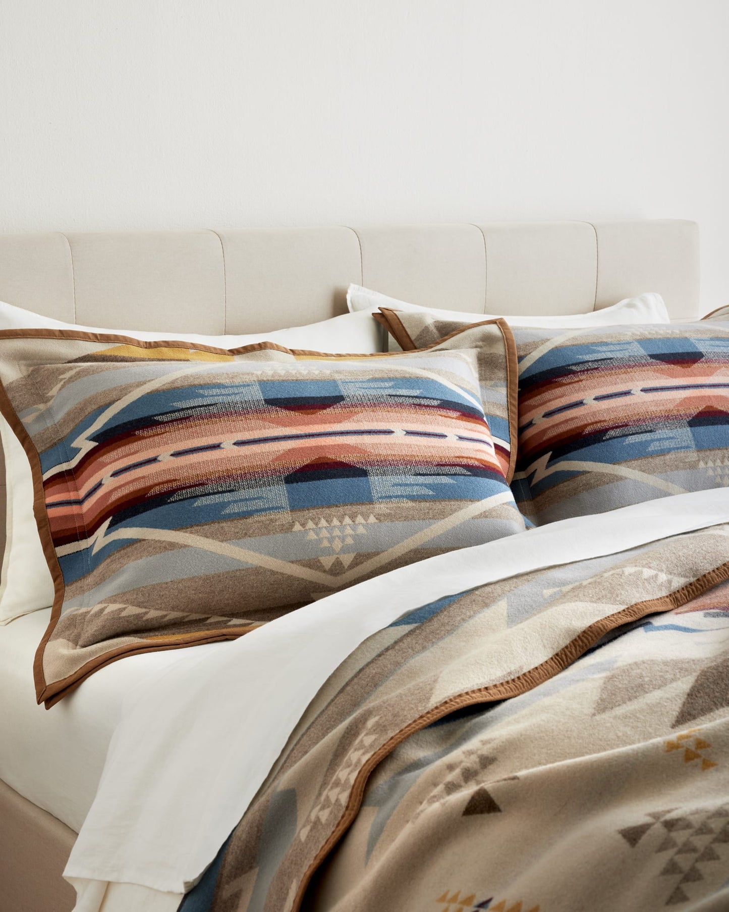 Patterned pillows and blanket on a bed with a neutral headboard