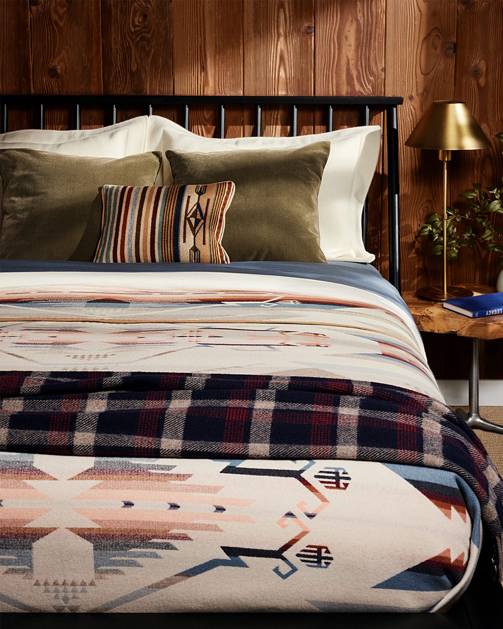 Bed with patterned bedding and pillows in a room with wooden walls and a lamp.