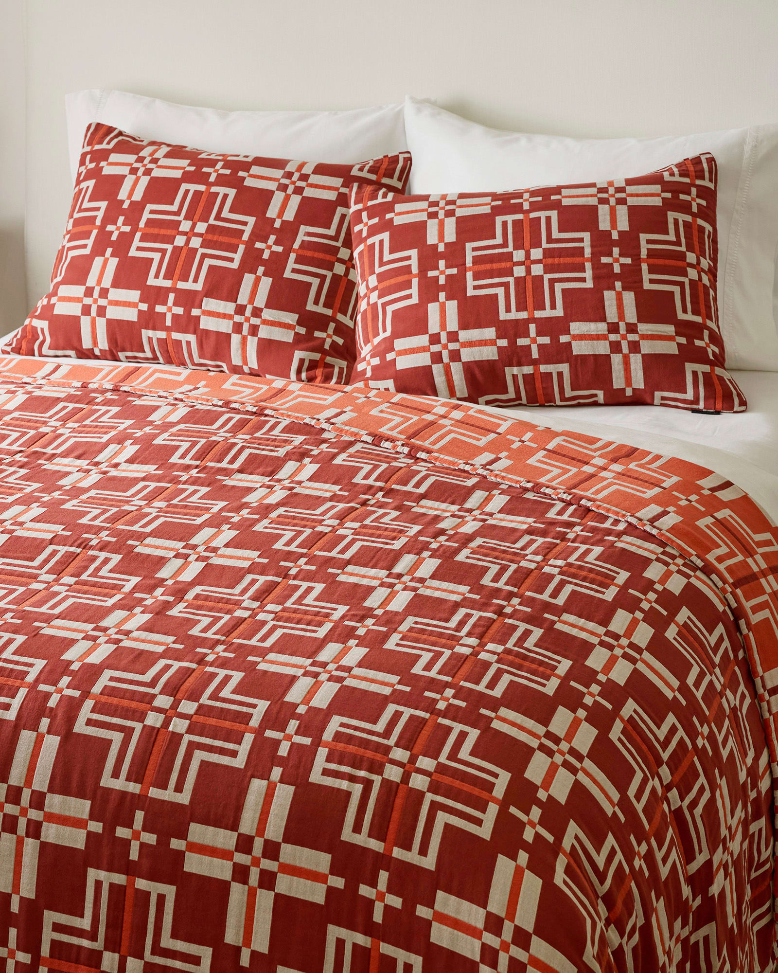 Red and white geometric patterned bedding set on a bed with pillows.