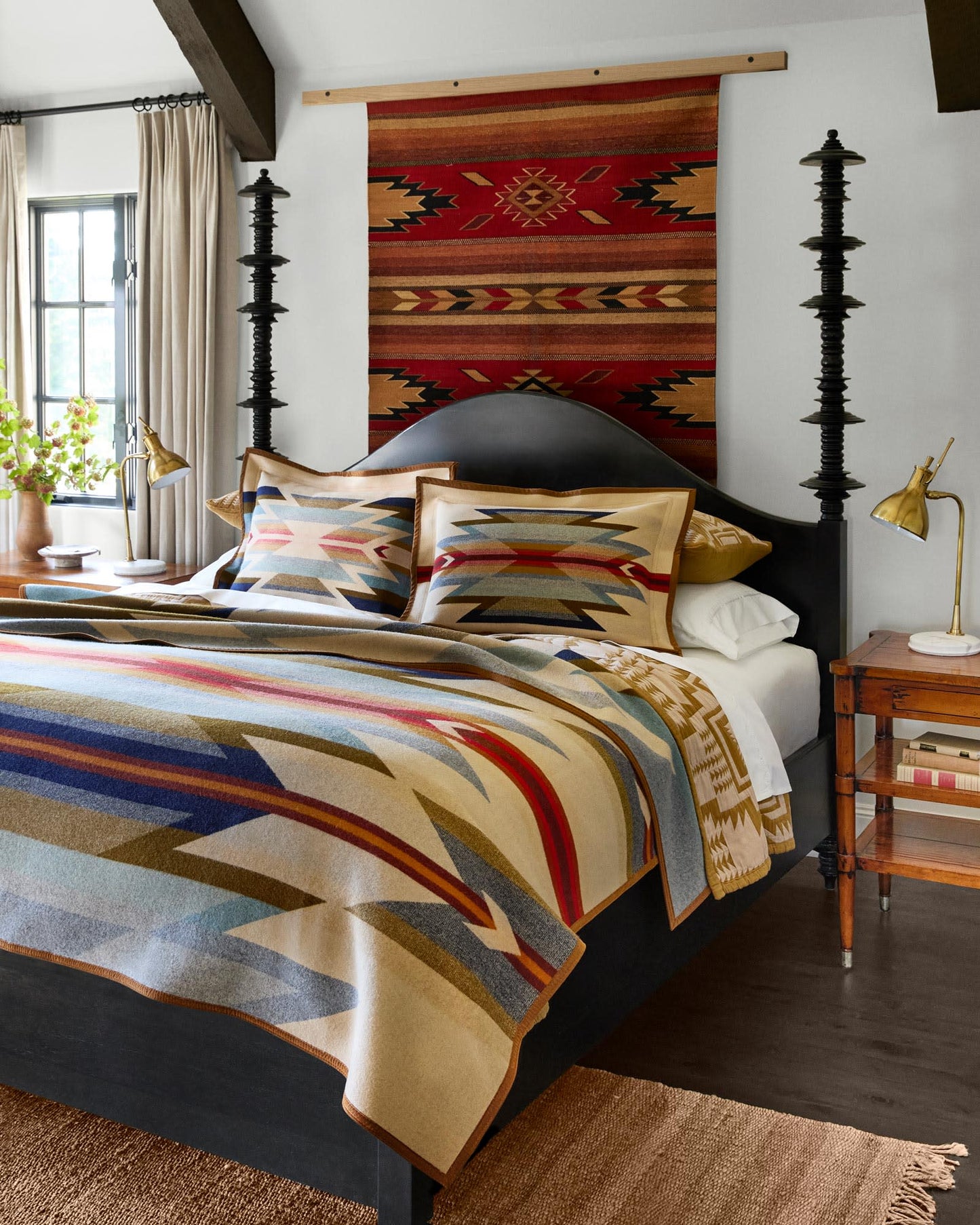 Bedroom with a bed featuring patterned bedding, pillows, and a rug on the wall.
