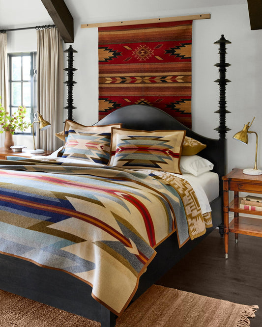 Bedroom with a bed featuring patterned bedding, pillows, and a rug on the wall.